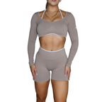 Person wearing a beige long-sleeve athletic top and shorts set on a white background